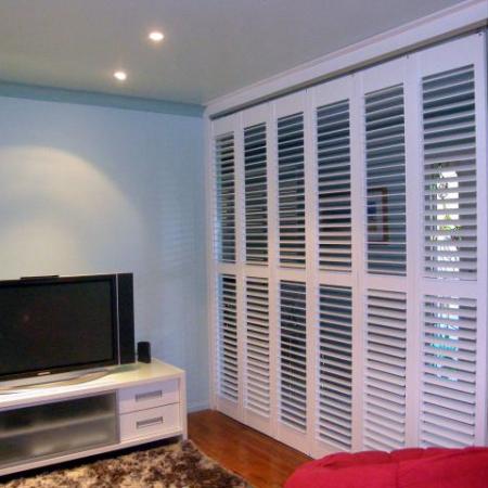 Stylish in white: Plantation Shutters look good in any location. Leah's Painted Shutters brightens the room dramatically and contrasts well against the dark furniture. This room has sliding shutters; creating the perfect media room when needed.